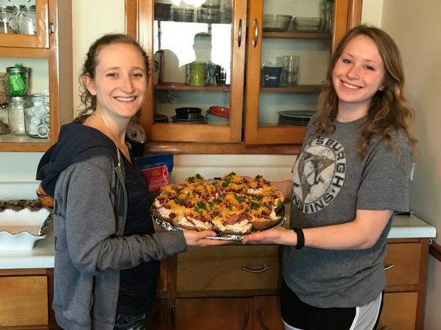 Girls holding tray of twice baked potatoes ready to go into oven