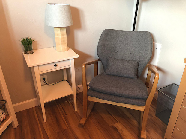 Gray rocking chair and white side table in baby girl nursery
