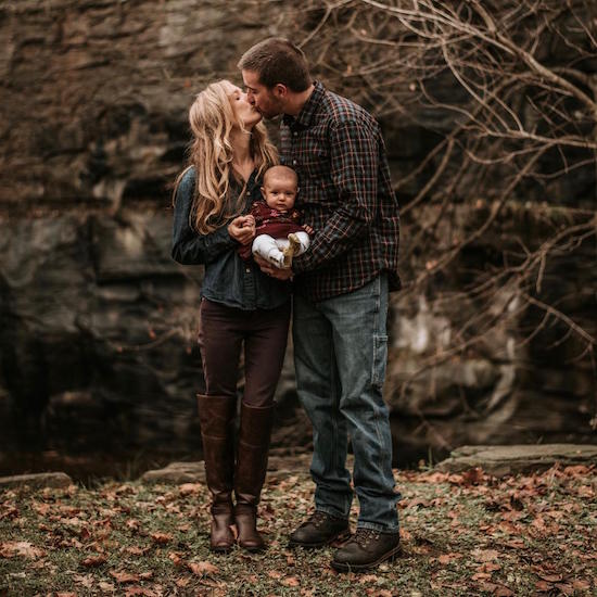 Husband and wife kissing and holding baby family photo