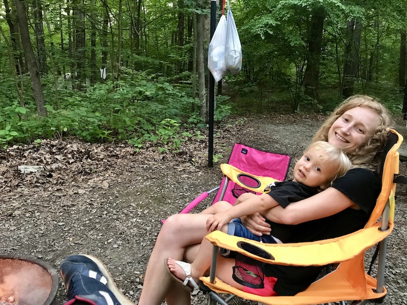 Mom and toddler sitting in camp chairs by campfire while camping