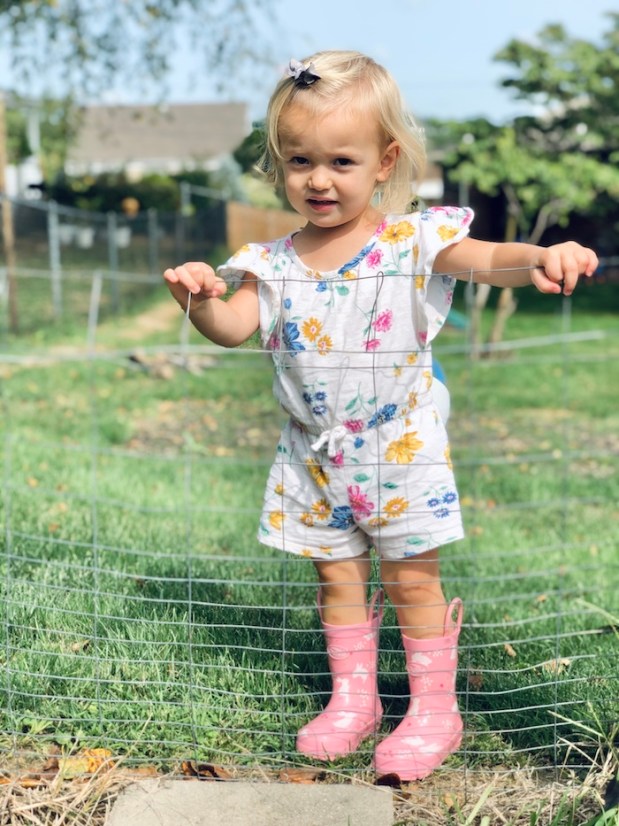 Toddler girl wearing romper and rain boots by garden