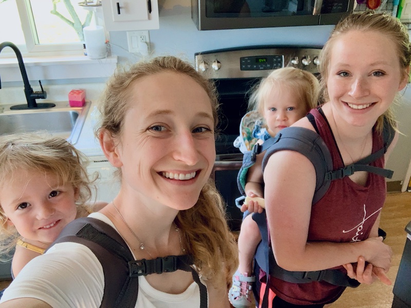 Sisters with their babies in carriers on their backs