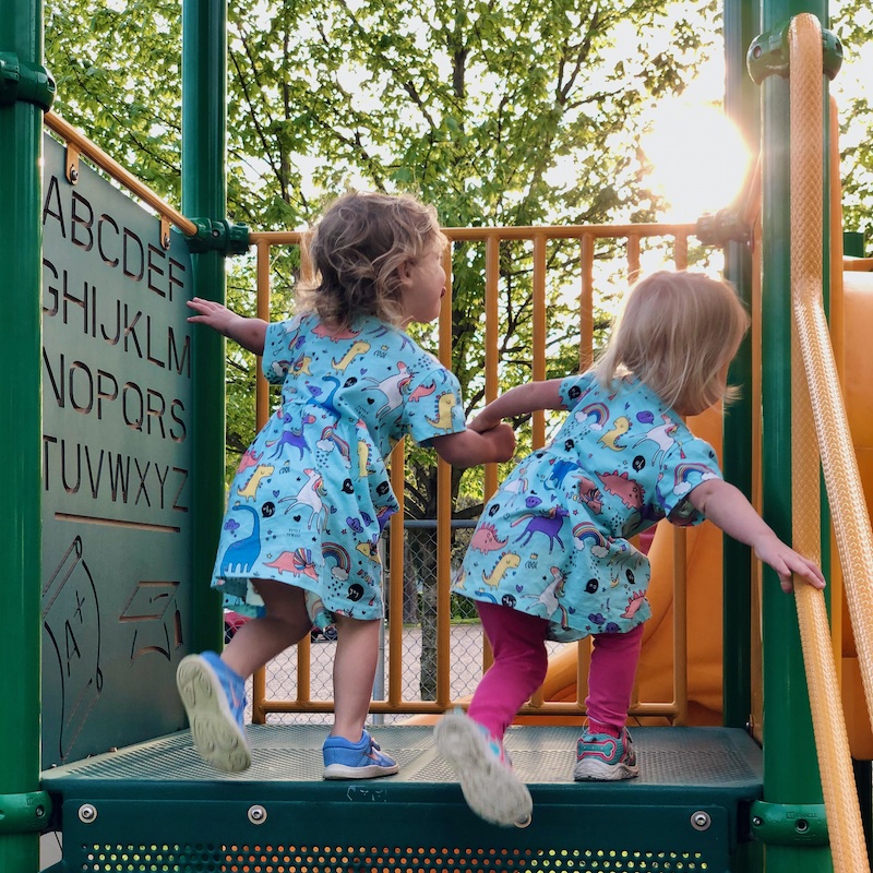 Toddler girls wearing matching dresses and holding hands at playground