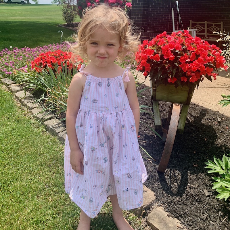 Toddler in dress standing by flowers and smiling