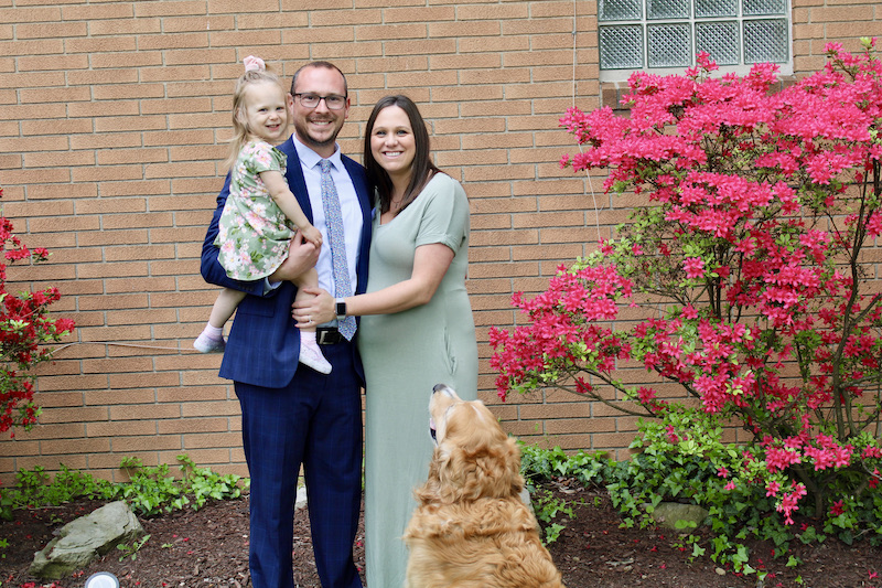 Husband and pregnant wife holding toddler daughter with golden retriever 