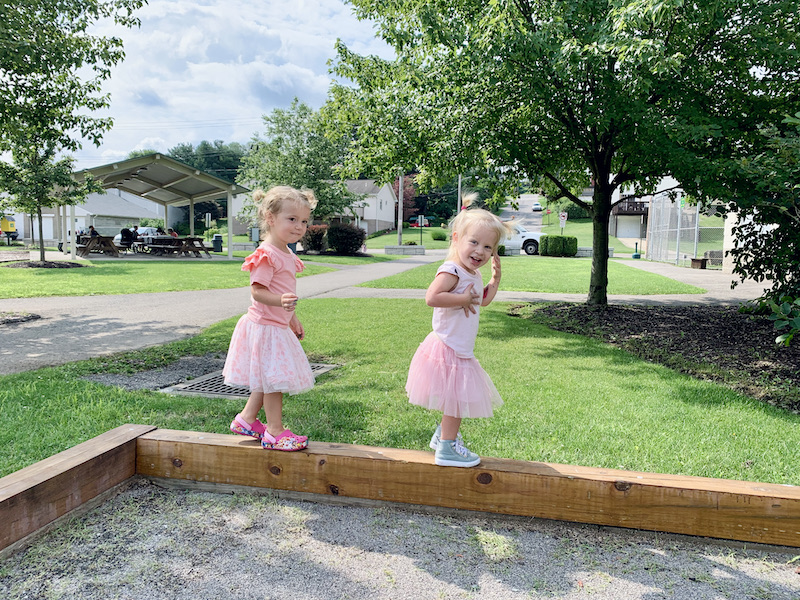 Toddler girls in matching outfit walking on wood beam