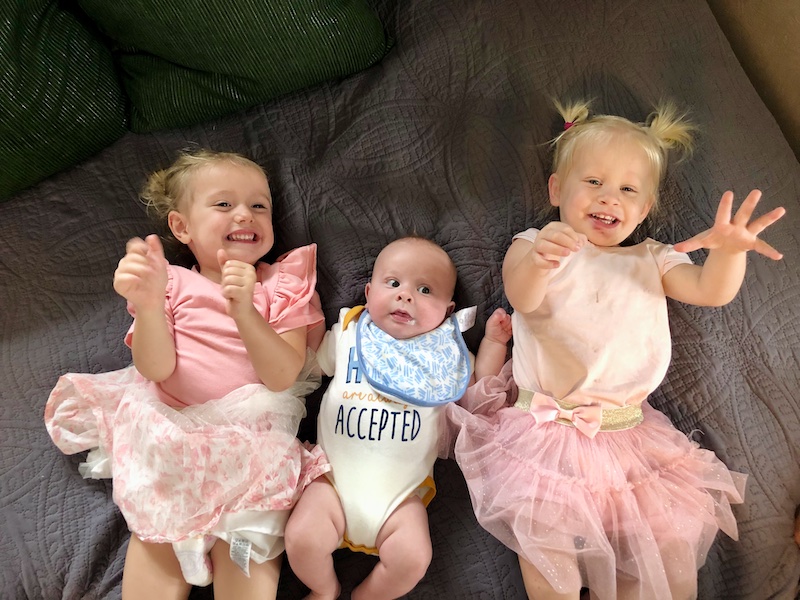 Toddler girls in matching tutu outfits and baby boy all laying together on bed