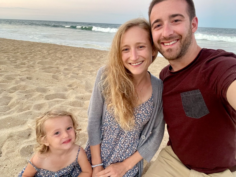 Mom and dad with toddler daughter sitting in the sand at the beach in Outer Banks, NC
