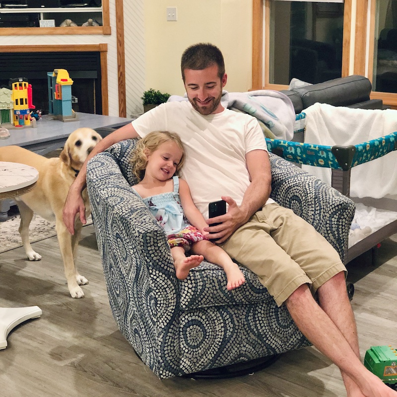 Father and daughter sitting on couch together and smiling at phone.