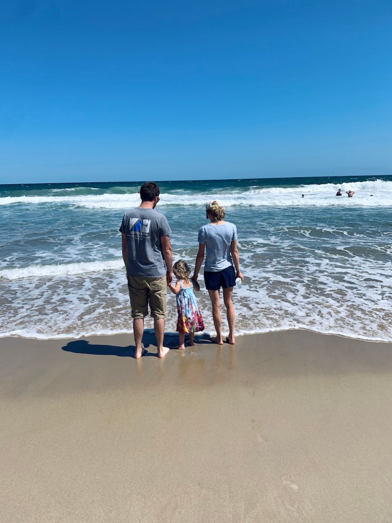 Mom and dad holding toddler girls's hands at the beach in the Outer Banks of North Carolina.