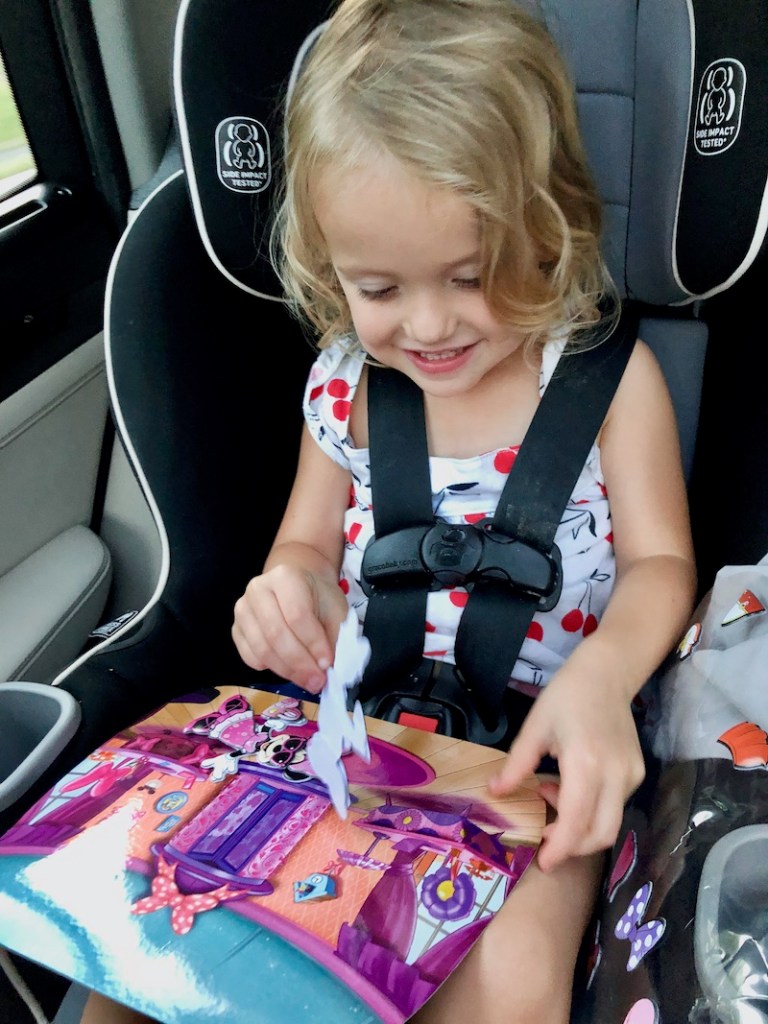 Toddler playing with Minnie Mouse puffy sticker playset in carseat.