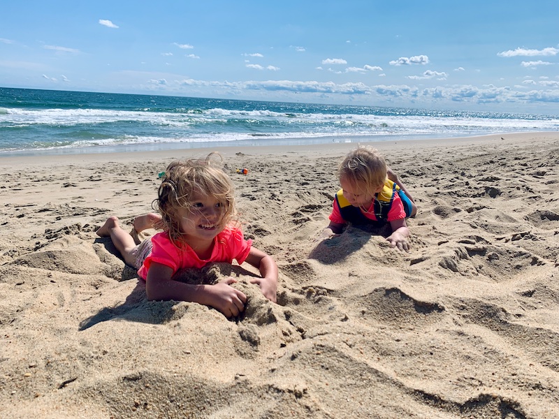 Toddler girls on the beach laying in the sand in the Outer Banks