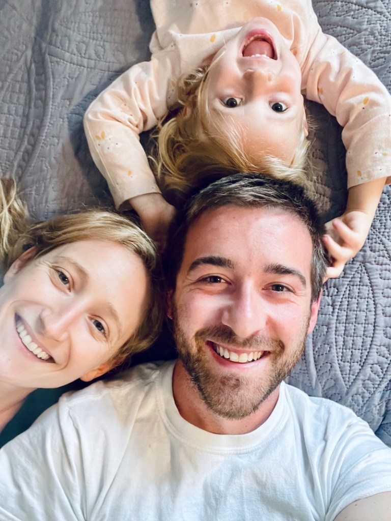 Mom and dad with daughter laying on bed smiling for selfie