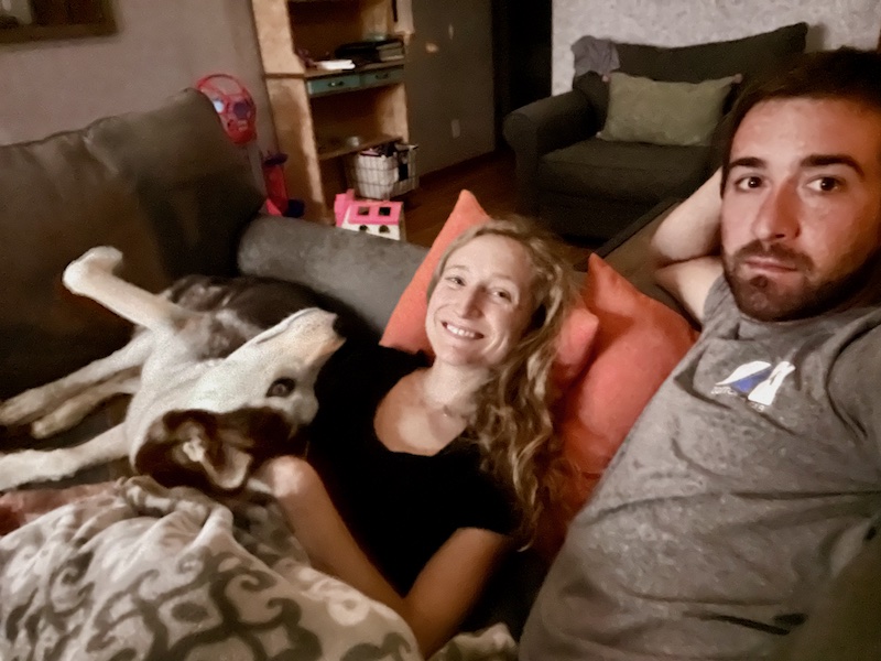 Husband and wife snuggling on couch with husky