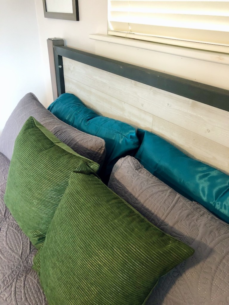 Green, gray, and teal pillows on king sized bed with homemade steel and wood headboard