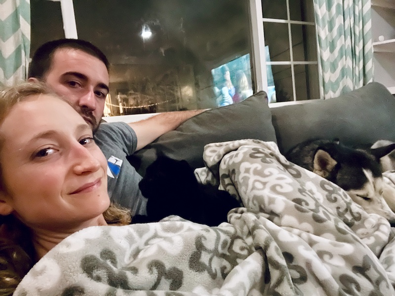 Husband and wife snuggling on couch with husky and cat