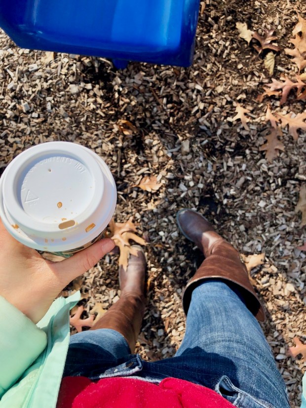 Girl wearing brown boots and holding a Starbucks coffee at park