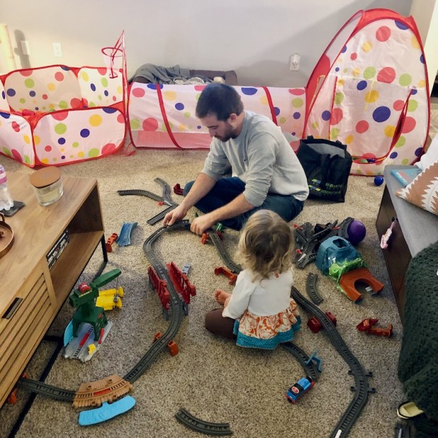 Dad and toddler playing with train set on floor