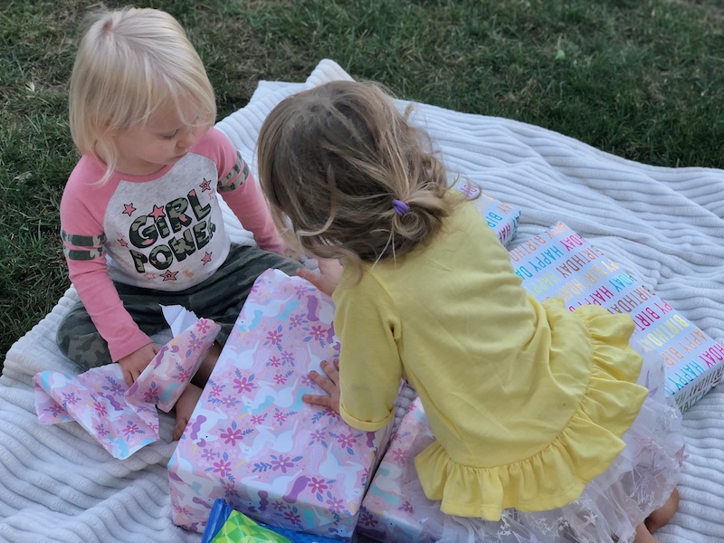 Toddler girls opening gifts on a blanket outside in the grass