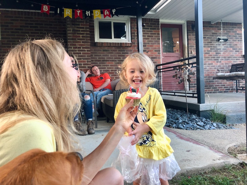 Toddler girl smiling after blowing out three birthday candles on a strawberry cupcake