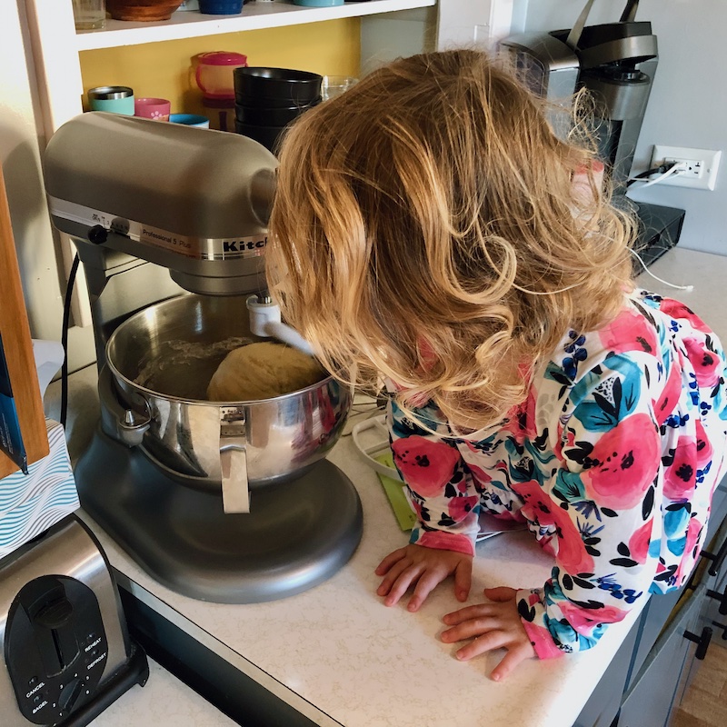 Toddler girl sitting on counter looking at kitchenaid mixer making bread