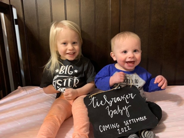 Toddler sister and brother holding sign announcing new baby