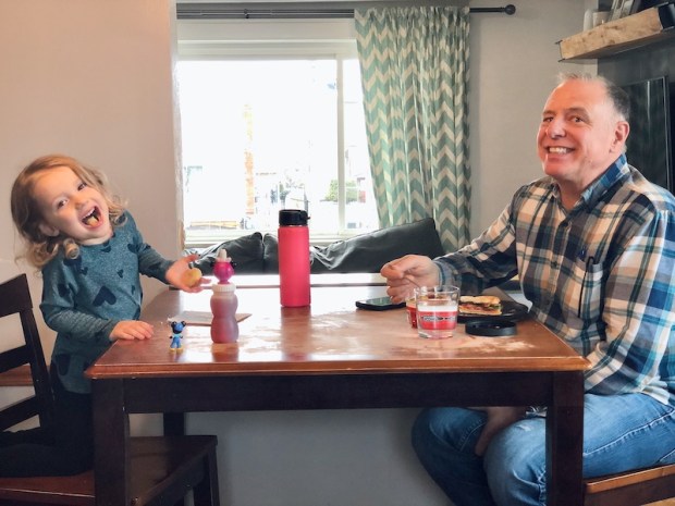 Toddler girl and grandpa sitting at kitchen table eating together
