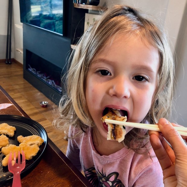 Toddler girl eating Korean potato pancakes with chopsticks