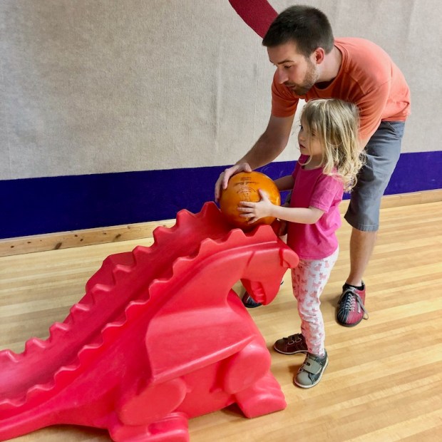 Dad teaching toddler daughter how to bowl