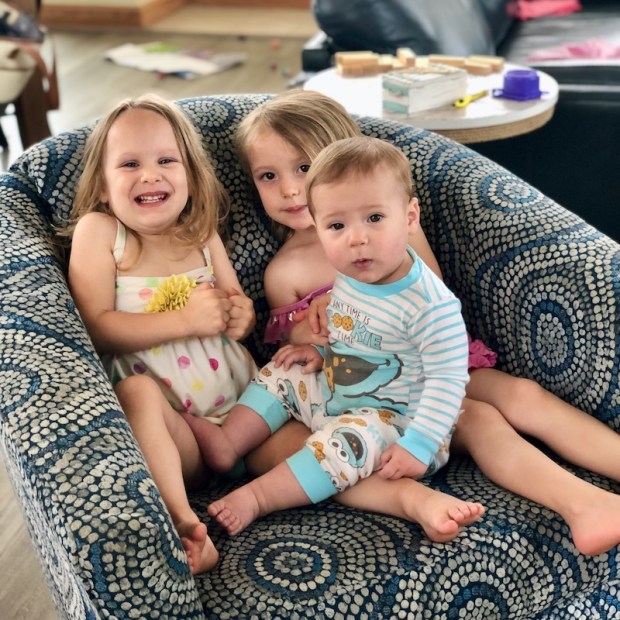 Two toddlers and baby cousin sitting on blue couch together