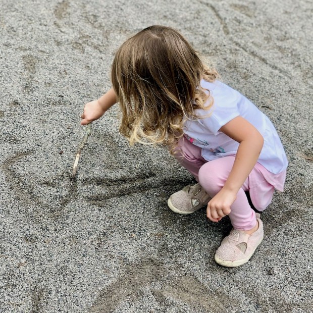 Little girl playing in sand with stick
