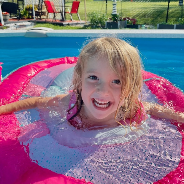 Young girl swimming in a pool with pink raft