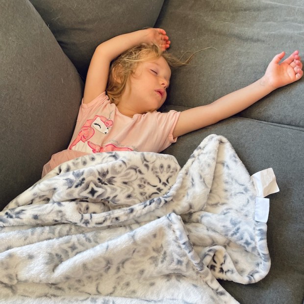 Girl in pink dress napping on couch with arms over head