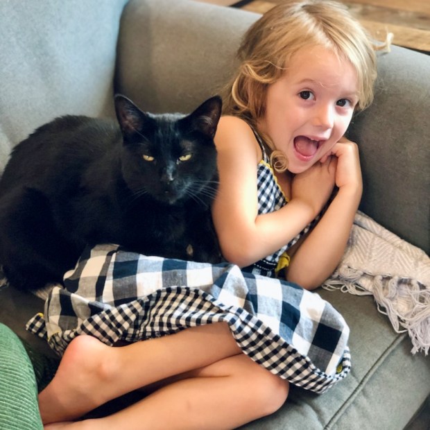 Black cat sitting on girl on couch