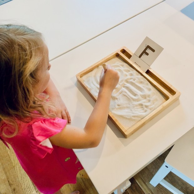 Child using Montessori sand tray to learn to write letters of the alphabet
