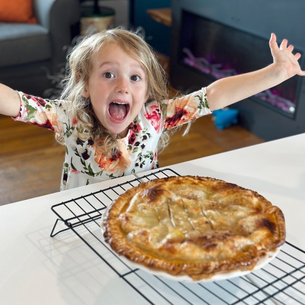 Girl with arms out standing behind apple pie