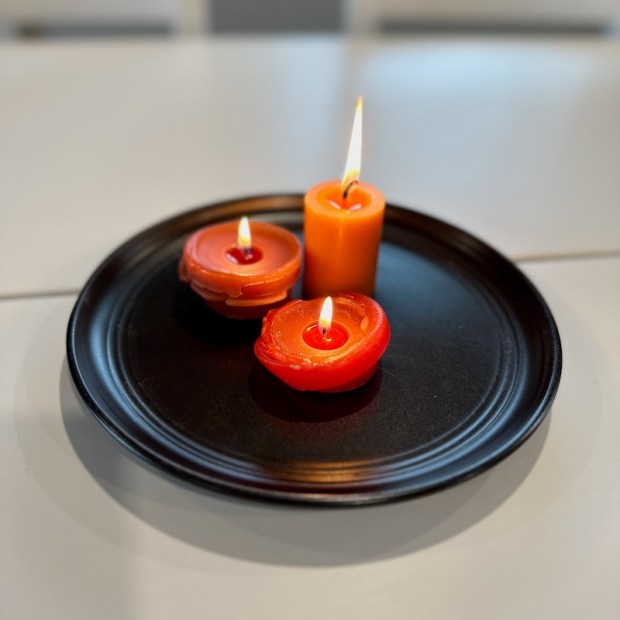 Orange pumpkin-scented votive candles burning on a black plate