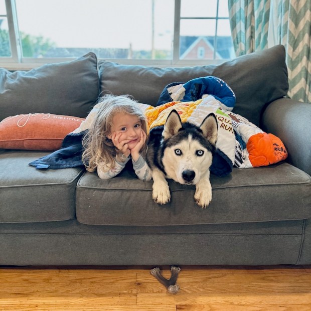 Child and husky snuggling under blanket on couch