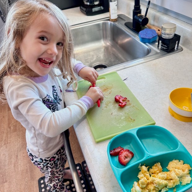 Four year old standing on step stool while cutting strawberries