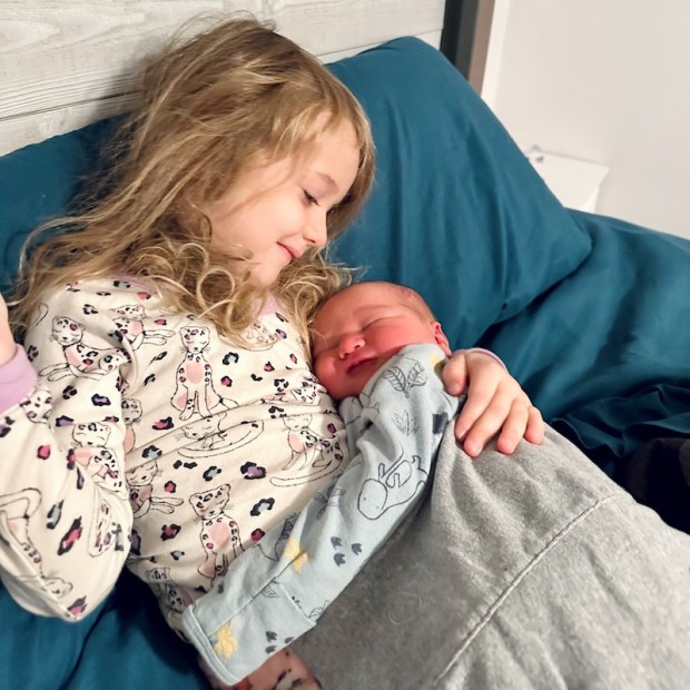 Big sister holding newborn little brother on her chest in bed