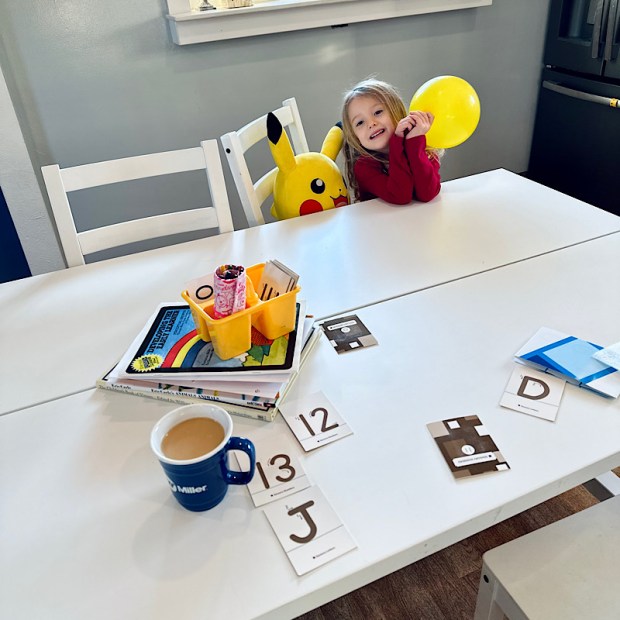 Young girl sitting at kitchen table with Pikachu stuffed animal