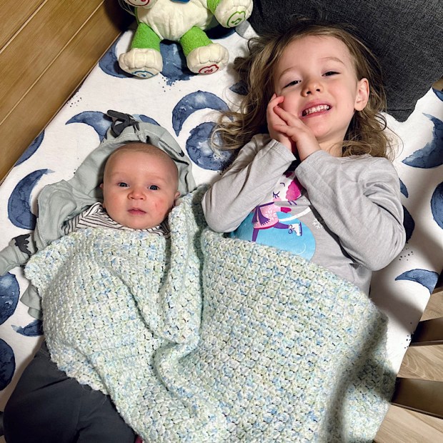 Girl laying with baby brother in crib