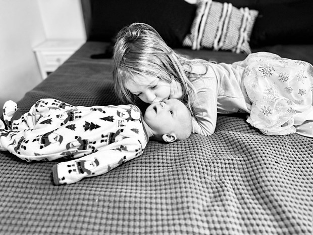 Big sister kissing baby brother black and white photo on bed