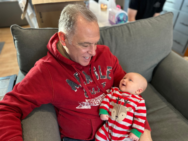 Grandpa holding newborn grandson on couch at Christmastime