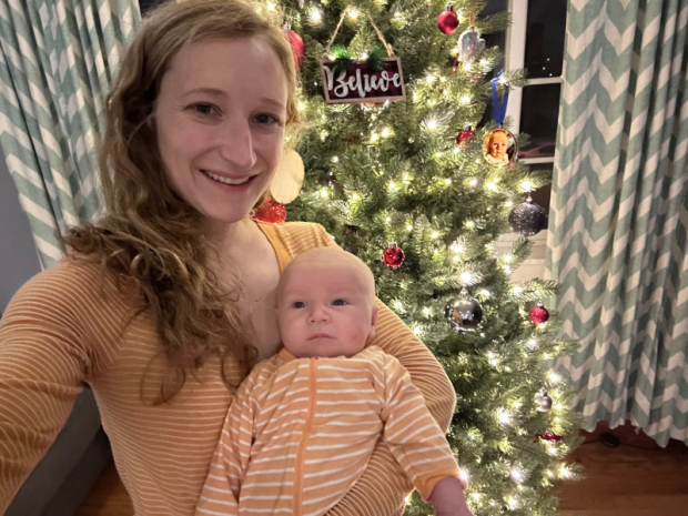 Mom holding newborn baby in front of Christmas tree