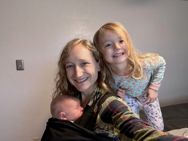 Mom with newborn in baby wrap carrier standing by preschooler in pajamas