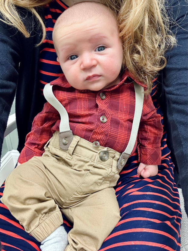 Baby boy wearing suspenders and red shirt sitting on mom's lap