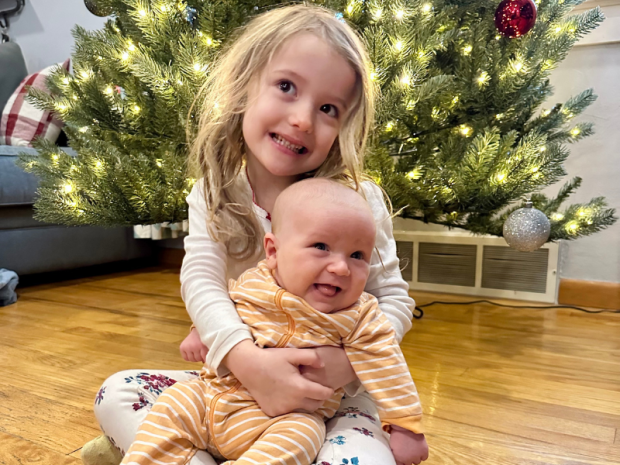 Older sister holding baby brother in front of Christmas tree