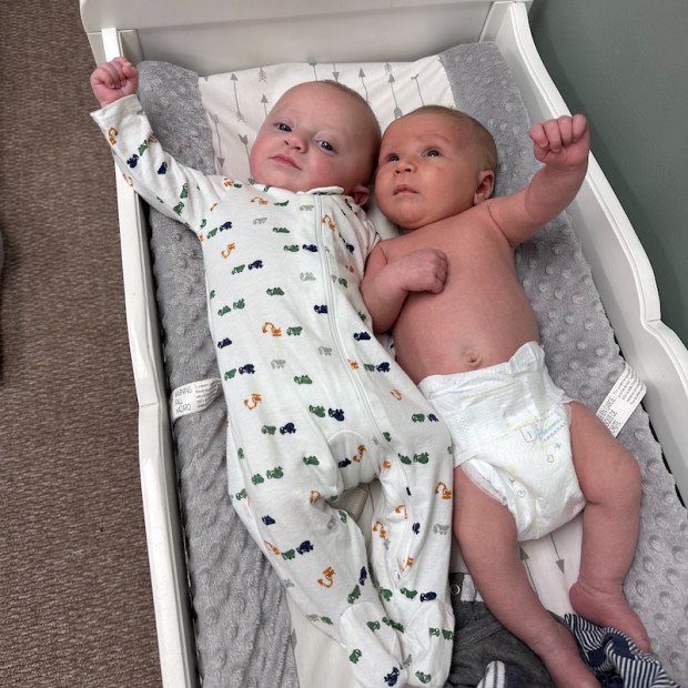 Baby boys laying on changing table with arms up in bro fist