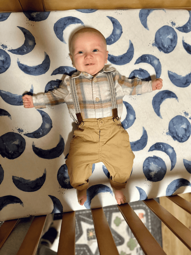 Two month old baby boy laying in crib in suspenders and button down shirt